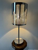 Front view of illuminated lamp showing entire cylindrical shade with Twin Towers skyline and chrome base