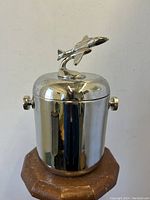 Front view of nickle plated cylinder ice bucket with airplane finial lid.