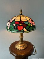 Photo showing full lamp with dome-shaped stained glass shade in floral design and brass hexagonal base.