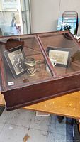 Close-up photo showing angled glass top with rippled original period glass and wooden frame, containing framed photos and a small metal object (not included in sale).