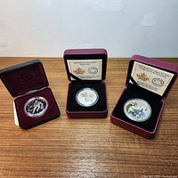 Three silver coins in their display cases: $1 coin at left, $10 Maple Leaf in centre, $20 coloured Nanabozhoo at right