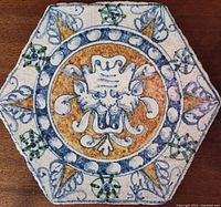 Close-up of hexagonal ceramic tile with central sea monster face design showing colors and crackle glaze