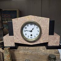 Front view of the pink marble Art Deco mantle clock showing the round white clock face with black numbers and brass bezel, resting on a wooden surface with a key in front.