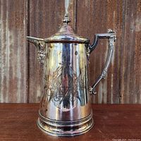 Front angle view of large antique silverplated water pitcher with ornamental handle and hinged lid.