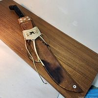 Large cutter knife in sheath lying on wooden surface.