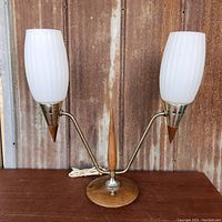 Front-facing image of the lamp showing both milk glass shades, brass arms, and walnut base with central wood accent.