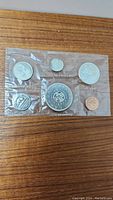 Photo showing front of sealed coin set in cellophane with all seven coins visible arranged with larger coins in middle and smaller around edges on wooden background.