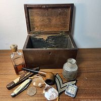 Georgian mahogany pipe box with interior showing original brass handle and metal lining remnants, along with pipe, eyeglasses, knives, coin, patch, watch, and bottles arranged on wooden surface