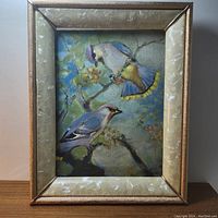 Frontal image of the art piece in frame showing two birds perched on a flowering tree branch with blue sky background.