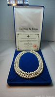 Front view of three-strand pearl necklace in blue velvet box with certificate.