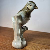 Full side view of bird figurine perched on stylized tree stump base with naturalistic paint detail in earthy tones.