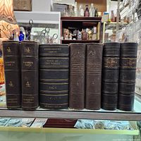 Front view of four faux book cover stereoview storage containers with gold embossed titles on black covers, displayed standing upright on shelf.