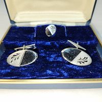 Close-up image of vintage sterling silver oval men's cufflinks and matching tieclip, all resting inside original blue velvet box. The cufflinks and tieclip show a leaf design on one half and polished finish on the other.