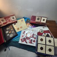 Multiple coin sets and presentation folders including silver coins in protective holders on a blue fabric.