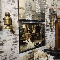 Pair of polished brass wall sconces mounted on a whitewashed brick wall, surrounded by mirrors and various antique furniture in a showroom setting.
