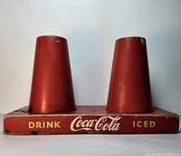 Front view of the vintage Coca Cola counter display showing two red cone-shaped holders and Coca Cola branding in yellow and white.