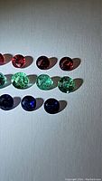 Twelve natural gemstones arranged on a light surface under varied lighting revealing their colors and cuts.