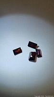 Four deep red almandine garnet gemstones with a fancy baguette cut on a plain white background under focused light.