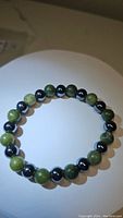Image showing natural green jade and metallic hematite beads in a stretchy beaded bracelet laid flat in a circular shape.