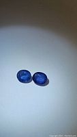 Pair of two natural oval cut blue sapphires on white background showing shape and color.