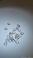 Group of small round cut clear white topaz gemstones spread on a surface under light showing clarity and size