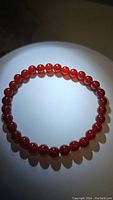 Carnelian bracelet displayed laid flat on a round white surface under focused lighting, showing the vibrant fire orange red color of uniformly round polished beads.