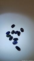 Top view of 11 oval cut natural sapphires with dark blue coloration and some inclusions visible.