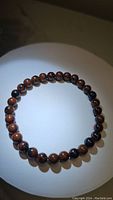 Full circular view of the mahogany jasper bracelet showing the round brown and black beads on a white background with shadow.