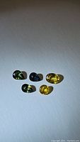 Five mixed colored natural sapphires on white background, showing color variety and shape.