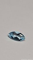 Marquis cut sky blue topaz gemstone lying flat, showing its bright blue color and faceted surface.