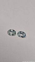 Two oval cut natural Cambodian zircon gemstones with soft blue color and clarity shown on neutral background.
