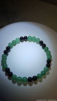 Front view of bracelet showing arrangement of green Aventurine and black Onyx beads in a circular shape under light.