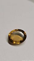 Oval cut golden champagne citrine gemstone on white background, showing facets and transparency.