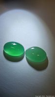 Two oval green aventurine cabochons placed side by side under focused light showing translucency and clarity.