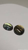 Two polished natural labradorite cabochons, one oval and one round, showing colorful flashes on white background.