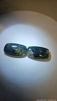 Pair of two cushion cabochon moss agate stones shown on a white surface under diffuse lighting to highlight color and pattern.
