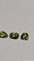 Three apple green natural peridot gemstones placed side-by-side showing their mixed faceted cuts and good clarity.