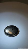 Oval cabochon shaped natural pyrite gemstone with golden metallic color, shown from one angle under direct light highlighting reflective surface and texture.
