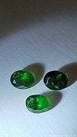 Three oval cut bright green tsavorite garnet gemstones under light on white background.