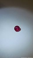 Close-up photo of the round cut, blood red natural ruby gemstone on white background, showing color and facet details.