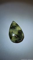 Teardrop semi-translucent green prehnite gemstone with rutilated inclusions, polished and reflecting light