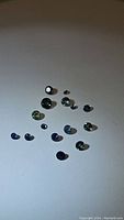 Photo showing 14 round cut natural sapphires in a variety of blue, green, and teal colors scattered on a white background.