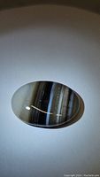Close-up of oval natural striped agate cabochon on white background showing details of banded pattern and polished surface.