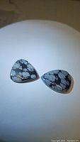 Two pear-shaped natural snowflake obsidian cabochons shown on a plain background, highlighting their classic black and white snowflake pattern.