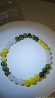 Top view of the round stretchy bracelet made with polished natural jade beads in green, white, and yellow, laid out fully visible in circular form.