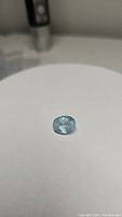 Photo of oval cut light blue aquamarine on white background, showing facets and natural inclusions.