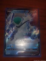 Holographic full art Ice Rider Calyrex V card showing character and text clearly, laying flat on wooden surface.