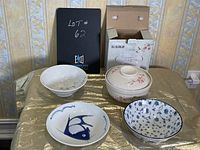 Lot of four decorative ceramic bowls arranged on table, one in box, one with lid visible showing floral designs and blue fish motifs