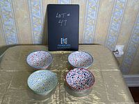 Four colorful ceramic bowls arranged in a square pattern with a box behind them, showing the overall set and pattern colors.