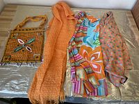 Photo showing all three scarves and the embellished cloth handbag placed horizontally on a surface.